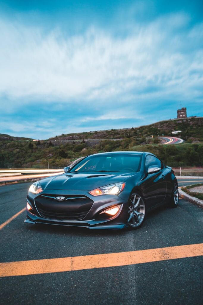 Luxury black vehicle with glossy surface and turned red headlights on paved road near slopes covered with grass and tiny tower on horizon in Canada